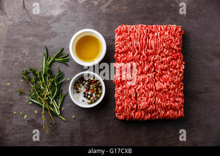 La viande hachée sur fond ardoise avec du poivre, l'huile et les herbes Banque D'Images