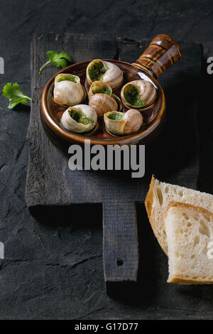 Escargots de Bourgogne escargots aux herbes - beurre, un plat gastronomique, en céramique traditionnel poêle avec le persil et le pain tranché sur woo Banque D'Images