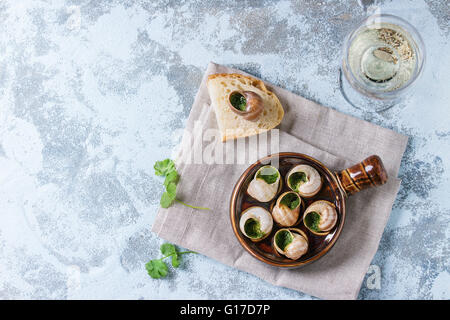 Escargots de Bourgogne escargots aux herbes - beurre, en céramique traditionnel poêle avec le persil, du pain et un verre de vin blanc sur tex Banque D'Images