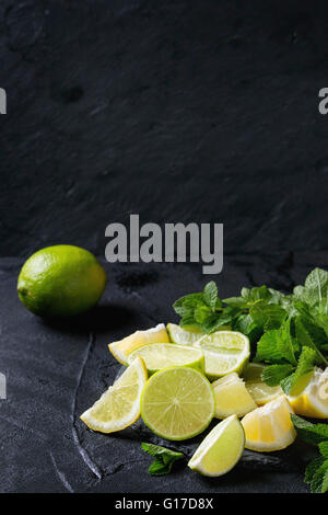 Tranches de Lime et de citrons avec bouquet de menthe fraîche sur l'ardoise noire sur fond texturé noir Banque D'Images