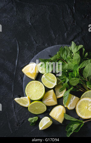 Tranches de Lime et de citrons avec bouquet de menthe fraîche sur l'ardoise noire sur fond texturé noir. Vue d'en haut. Banque D'Images