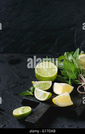 Tranches de Lime et de citrons avec bouquet de menthe fraîche sur la planche à découper en bois noir sur fond texturé noir Banque D'Images