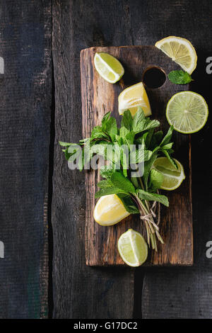 Tranches de Lime et de citrons avec bouquet de menthe fraîche sur la planche à découper en bois sur fond sombre. Vue d'en haut Banque D'Images