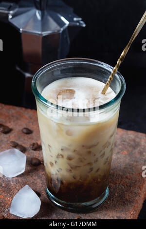 Verre de glace Café avec lait et crème, servi avec des grains de café, des cubes de glace et cafetière sur conseil de pierre noire sur b texturé Banque D'Images