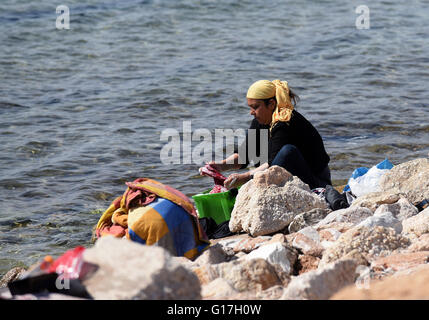 Une femme, qui vit dans un établissement accueillant des réfugiés à l'ancien aéroport d'Athènes, lave ses vêtements dans la mer Banque D'Images