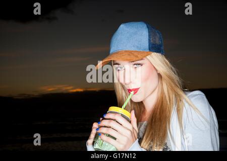 Jeune femme portant chapeau de base-ball de potable pot Mason smiling at camera Banque D'Images