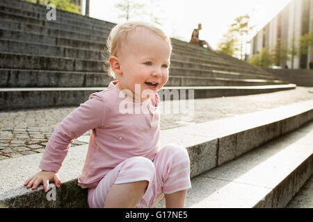 Petite fille, assis sur les marches, à rire, à l'extérieur Banque D'Images