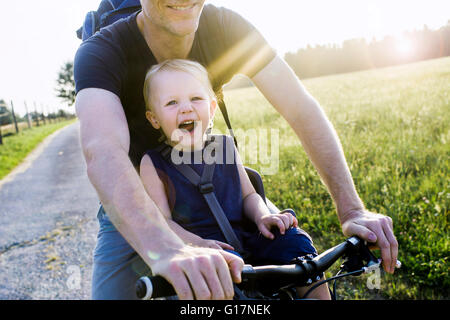 Père et fille de bébé riding bike ensemble, mid section Banque D'Images