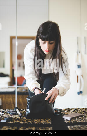 Jeune femme à la recherche de sac de maquillage dans la chambre Banque D'Images