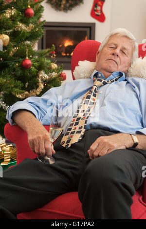 Senior man holding champagne flute endormi dans un fauteuil à Noël Banque D'Images