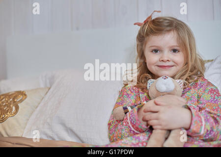 En pyjama fille hugging teddy bear in bed Banque D'Images