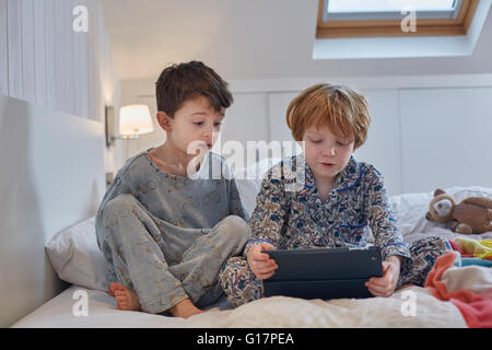 Les garçons en pyjama using digital tablet in bed Banque D'Images
