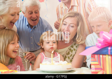 Baby Girl entouré par la famille blowing out bougie sur le gâteau d'anniversaire Banque D'Images