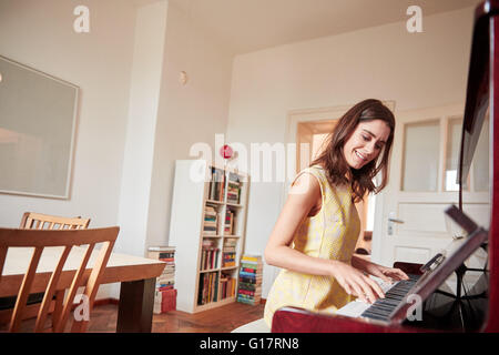 Jeune femme assise jouant du piano dans la salle à manger Banque D'Images