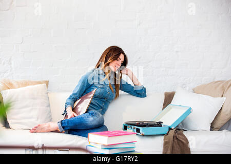 Jeune femme assise sur un canapé à écouter de la musique sur vintage record player Banque D'Images