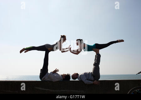 La silhouette symétrique des hommes et des femmes pratiquant le yoga acrobatique sur mur à la plage de Brighton Banque D'Images