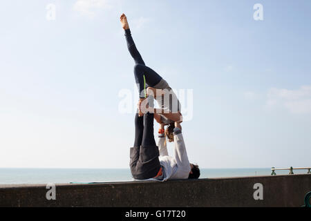 L'homme et la femme pratiquant le yoga acrobatique sur mur à la plage de Brighton Banque D'Images