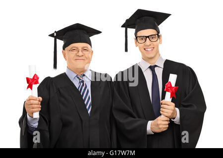 Mature et un jeune homme posant dans l'obtention du diplôme robes holding diplomas isolé sur fond blanc Banque D'Images