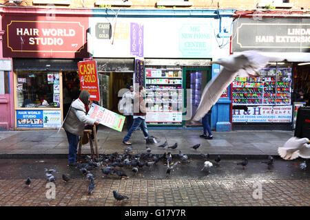 Scène de rue, Moore Street, Dublin, Irlande : un homme portant un panneau nourrit les oiseaux Banque D'Images