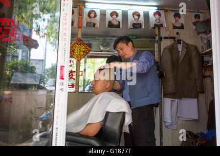 Entrepreneur chinois coiffure au travail avec un client à sa petite boutique de coiffeur, Nanjing, Chine Banque D'Images