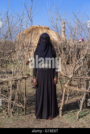 Une femme de l'Oromo éthiopiens habillés en noir de la burqa se tient devant sa hutte, région d'Amhara, Ethiopie, Artuma Banque D'Images