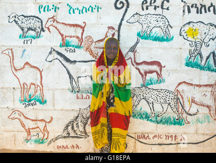 Tribu Nyangatom garçon enveloppé dans une écharpe de couleur en face d'une peinture murale de l'école, vallée de l'Omo, Ethiopie, Kangate Banque D'Images