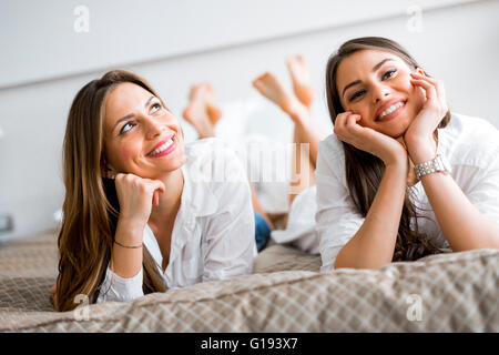 Deux belles filles talking and smiling couchée sur un lit luxueux Banque D'Images