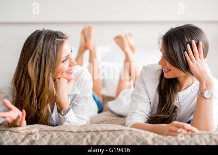 Deux belles filles talking and smiling couchée sur un lit luxueux Banque D'Images