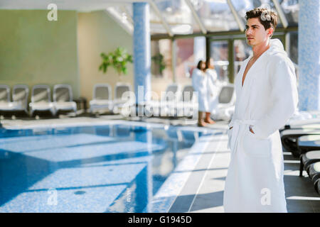 Homme debout à côté d'une piscine dans une robe et relaxant Banque D'Images