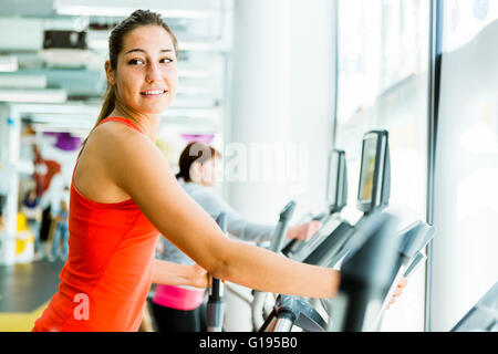 Jeune femme fit à l'aide d'un entraîneur elliptique dans un centre de remise en forme et souriant Banque D'Images