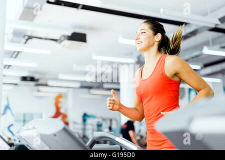 Belle jeune femme s'exécutant sur un tapis roulant dans une salle de sport et smiling Banque D'Images