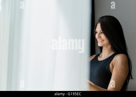 Heureux belle jeune femme regardant par la fenêtre Banque D'Images