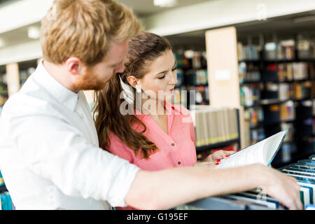 Deux étudiants intelligents la lecture et l'étude d'une recherche dans toute bibliothèque de livres sur les étagères Banque D'Images