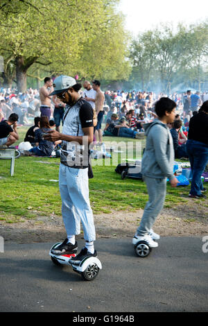 Hackney. Parc des champs de Londres. Dimanche après-midi au soleil. Jeune homme contrôler son téléphone debout sur un Segway hoverboard. Banque D'Images