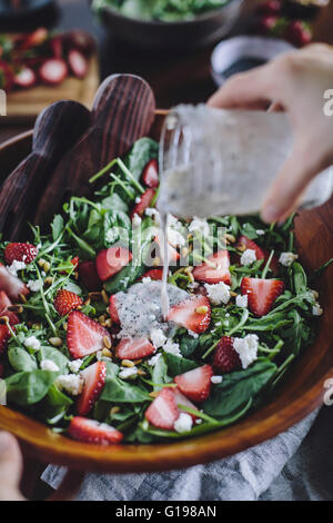 Une femme est photographié en versant vinaigrette aux graines de pavot dans une fraise et salade d'épinards. Banque D'Images