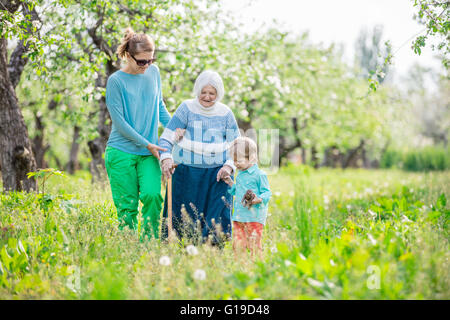 Senior woman soutenue par sa petite-fille et arrière-petit-fils de marcher dans les vergers en fleurs Banque D'Images