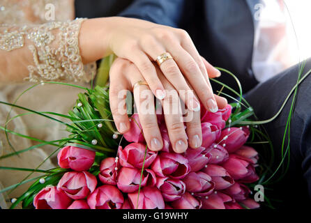 Les mains avec joints toriques Bride and Groom sur le mariage bouquet de rose Banque D'Images