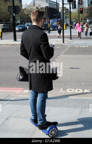 Un jeune homme vérifie son smartphone comme il tient en équilibre sur un scooter électrique sur le conseil d'Euston Road, à Londres, Angleterre, RU Banque D'Images