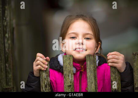 Portrait of little girl peeking de derrière la clôture. Banque D'Images