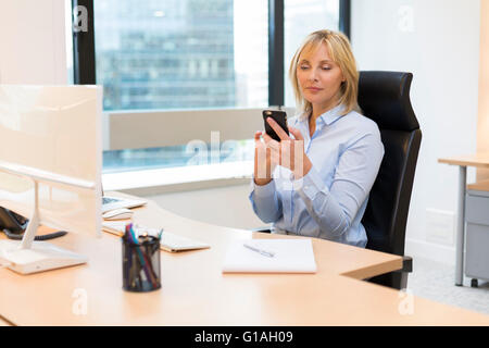 Femme d'affaires d'âge moyen travaillant au bureau. Using smartphone Banque D'Images
