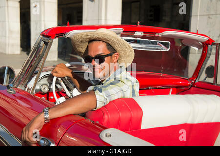 Jeune Cubaine un homme portant un chapeau de cowboy et des lunettes est assis à la place de conduite d'un 1950 classic car nous rouge à La Havane Cuba Banque D'Images