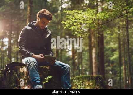 Beau jeune homme assis dans les bois et à l'aide d'un écran tactile numérique, connexion wi-fi et la liberté concept Banque D'Images
