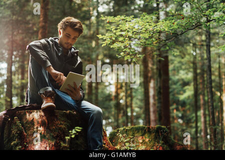 Beau jeune homme assis dans les bois et à l'aide d'un écran tactile numérique, connexion wi-fi et la liberté concept Banque D'Images