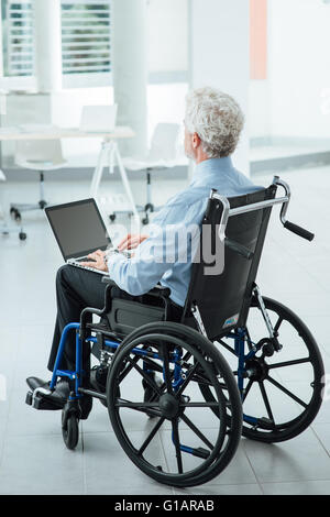 Homme d'entreprise réussie en fauteuil roulant à l'aide d'un bureau de travail et ordinateur portable Banque D'Images