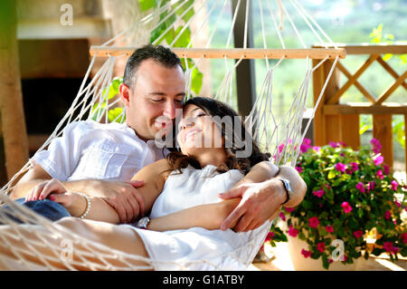 Portrait jeune couple vêtu de blanc sur un hamac de corde sur la terrasse d'une maison de campagne à la recherche d'amour Banque D'Images