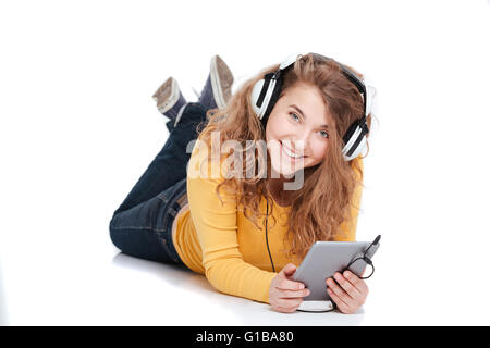 Smiling woman in headphones lying on the floor with tablet computer and looking at camera Banque D'Images