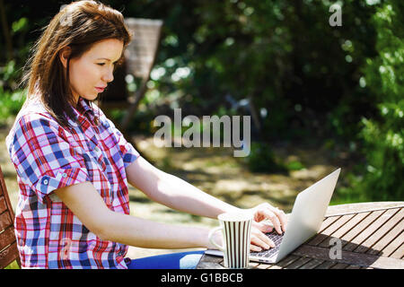 Portrait d'une femme à l'extérieur de travailler sur un ordinateur portable avec une tasse de thé ou de café Banque D'Images