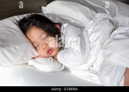 Petite fille dormir dans le lit avec couverture blanche. Banque D'Images
