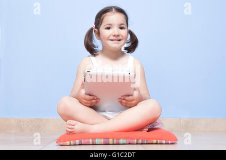 Smiling little girl sitting in her room floor using tablet computer Banque D'Images