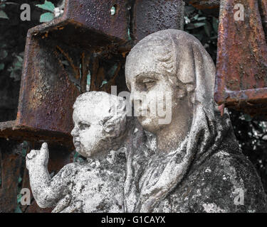 Mère Marie et Jésus dans un cimetière Italien ; la sculpture est entourée d'une croix rouillée. Banque D'Images